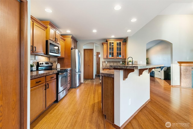 5983 Honeycutt Ct, Ferndale, WA 98248 - kitchen with appliances with stainless steel finishes, a kitchen bar, brown cabinets, arched walkways, and light wood-style flooring