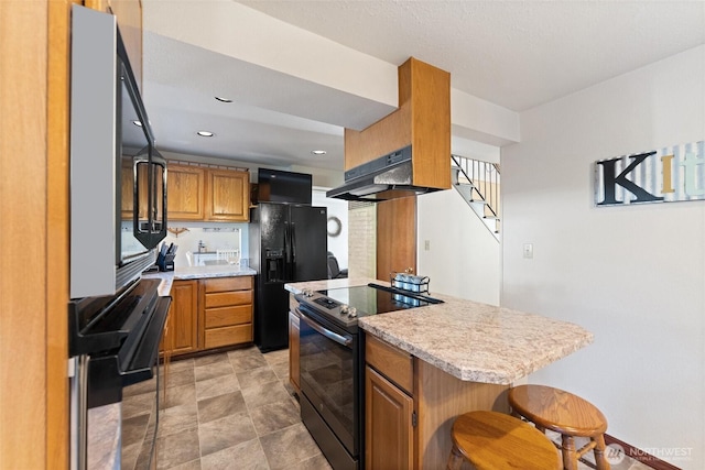 17310 Palatine Ave N, Shoreline, WA 98133 - kitchen with black appliances, under cabinet range hood, brown cabinetry, stone finish floors, and a breakfast bar area