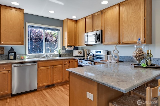 7332 156th St SE, Snohomish, WA 98296 - kitchen featuring appliances with stainless steel finishes, a peninsula, a kitchen breakfast bar, light wood-style floors, and light stone countertops