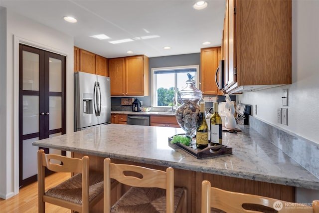 7332 156th St SE, Snohomish, WA 98296 - kitchen with appliances with stainless steel finishes, a peninsula, light stone counters, brown cabinets, and recessed lighting