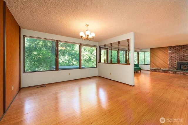 18707 25th Ave NE, Lake Forest Park, WA 98155 - unfurnished living room with a chandelier, light wood-style flooring, a textured ceiling, healthy amount of natural light, and a fireplace
