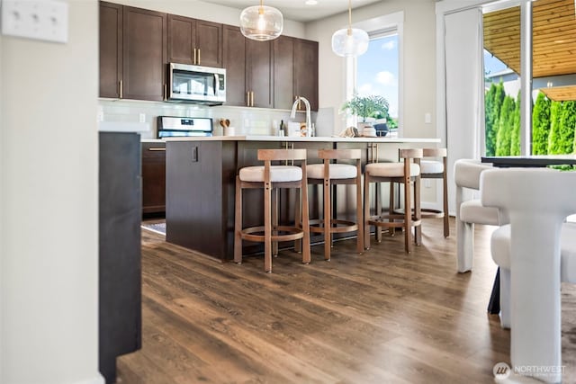 605 26th Avenue Ct, Milton, WA 98354 - kitchen featuring stainless steel microwave, tasteful backsplash, dark wood-style floors, light countertops, and a kitchen breakfast bar