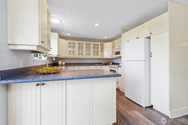 1418 W Mukilteo Blvd, Everett, WA 98203 - kitchen with white appliances, dark countertops, a peninsula, glass insert cabinets, and dark wood finished floors