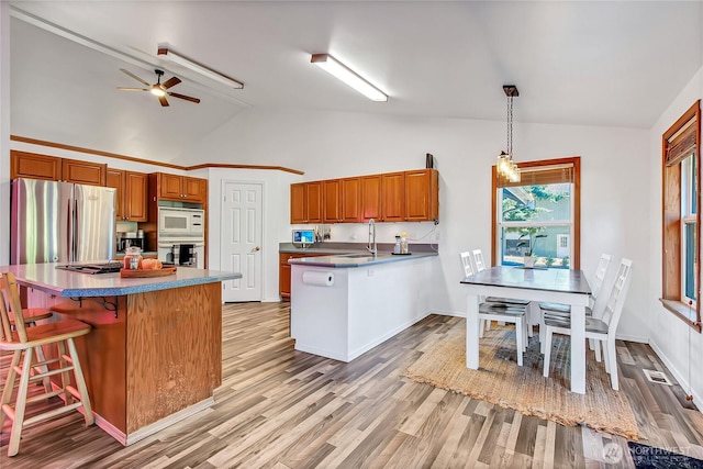 12310 Morris Rd SE, Yelm, WA 98597 - kitchen featuring stainless steel appliances, vaulted ceiling, a peninsula, a breakfast bar area, and brown cabinetry