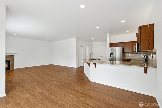 7022 Raptor Ave NE, Lacey, WA 98516 - kitchen featuring stainless steel fridge, light stone counters, a peninsula, a kitchen breakfast bar, and wood finished floors