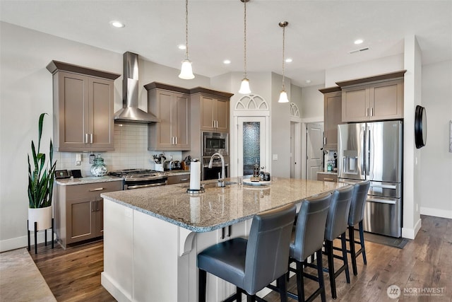 9511 W Floyd Dr, Cheney, WA 99004 - kitchen featuring stainless steel appliances, wall chimney exhaust hood, light stone countertops, backsplash, and a center island with sink