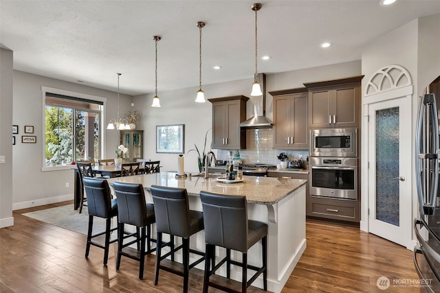 9511 W Floyd Dr, Cheney, WA 99004 - kitchen with appliances with stainless steel finishes, wall chimney range hood, dark wood finished floors, a kitchen breakfast bar, and recessed lighting