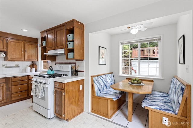 7147 29th Ave SW, Seattle, WA 98126 - kitchen featuring white gas stove, under cabinet range hood, brown cabinetry, open shelves, and tasteful backsplash