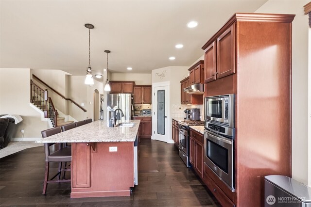 17116 138th Ave E, Puyallup, WA 98374 - kitchen with appliances with stainless steel finishes, under cabinet range hood, a kitchen breakfast bar, open floor plan, and light stone counters