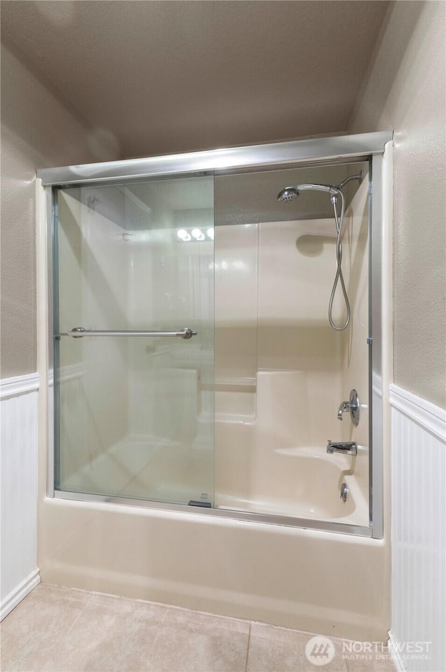 7511 Kittiwake Dr SE, Olympia, WA 98513 - bathroom featuring combined bath / shower with glass door, wainscoting, tile patterned flooring, and a decorative wall