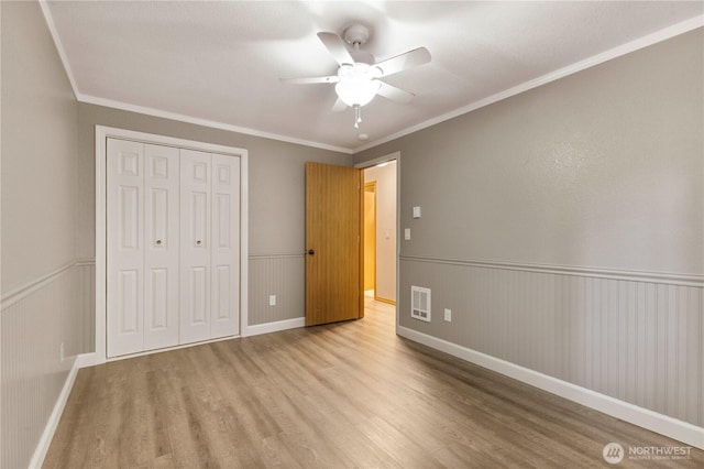 7511 Kittiwake Dr SE, Olympia, WA 98513 - unfurnished bedroom featuring wood finished floors, a closet, a wainscoted wall, crown molding, and ceiling fan