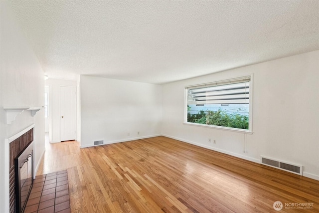 14326 Meridian Ave N, Seattle, WA 98133 - unfurnished living room with a tiled fireplace, light wood-style flooring, and a textured ceiling