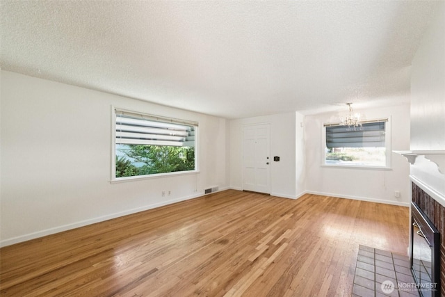 14326 Meridian Ave N, Seattle, WA 98133 - unfurnished living room with a chandelier, light wood-style floors, a textured ceiling, and a fireplace with flush hearth