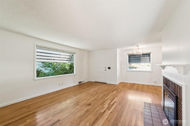14326 Meridian Ave N, Seattle, WA 98133 - unfurnished living room featuring a chandelier, plenty of natural light, a fireplace, light wood-style flooring, and a textured ceiling