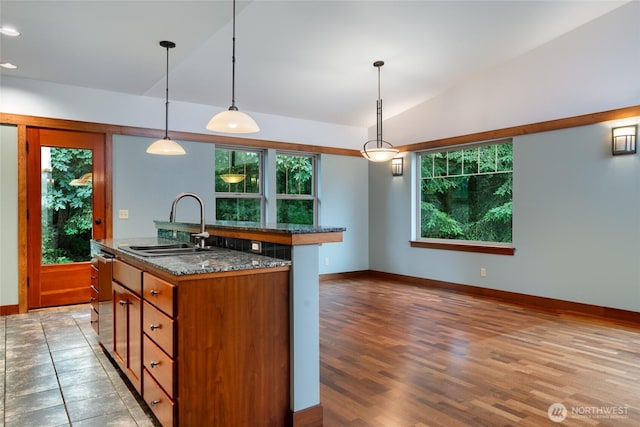 14450 Austin Pl, Anacortes, WA 98221 - kitchen with brown cabinets, stainless steel dishwasher, a kitchen island with sink, decorative light fixtures, and dark stone countertops