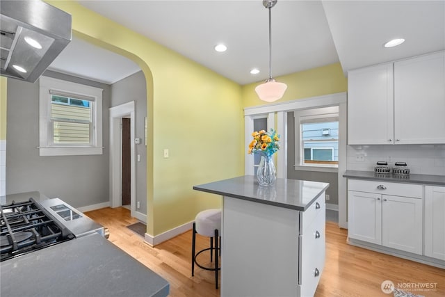 1531 NW 62nd St, Seattle, WA 98107 - kitchen with wall chimney exhaust hood, a kitchen island, white cabinetry, light wood-type flooring, and arched walkways