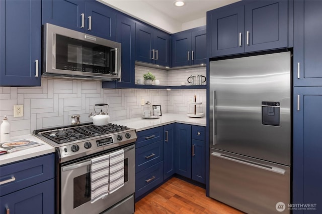 7549 SE 29th St Unit 305, Mercer Island, WA 98040 - kitchen with appliances with stainless steel finishes, blue cabinetry, light countertops, backsplash, and wood finished floors