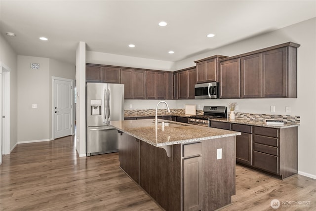 2846 Anna St NE, Lacey, WA 98516 - kitchen featuring stainless steel appliances, dark brown cabinetry, light stone countertops, a kitchen island with sink, and light wood finished floors