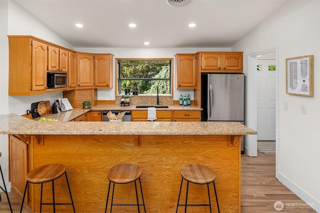 16223 NE 26th St, Bellevue, WA 98008 - kitchen with appliances with stainless steel finishes, a peninsula, light wood-type flooring, light stone countertops, and a kitchen breakfast bar