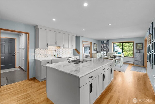 10212 SW 127th St, Vashon, WA 98070 - kitchen with light wood-style flooring, light stone counters, a center island, tasteful backsplash, and black electric cooktop