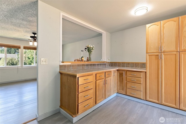 5701 38th Ct SE, Lacey, WA 98503 - kitchen featuring tile countertops, light wood finished floors, a ceiling fan, light brown cabinetry, and a textured ceiling