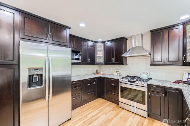 14111 NE 63rd Ct, Redmond, WA 98052 - kitchen featuring appliances with stainless steel finishes, wall chimney range hood, light wood-style flooring, dark brown cabinets, and light stone counters