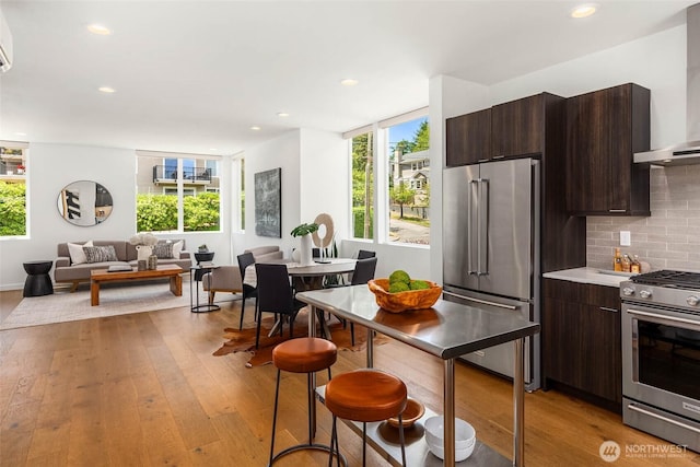 1918 5th Ave N Unit B, Seattle, WA 98109 - kitchen with appliances with stainless steel finishes, wall chimney range hood, dark brown cabinets, light wood finished floors, and recessed lighting