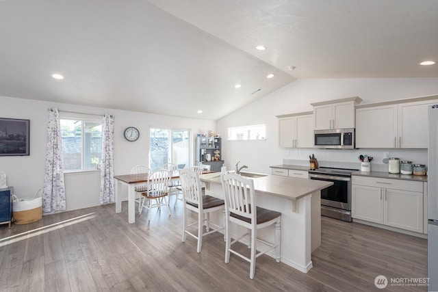 1205 W Sequoia Rd, Moses Lake, WA 98837 - kitchen with appliances with stainless steel finishes, lofted ceiling, wood finished floors, an island with sink, and a kitchen bar