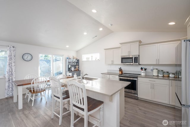1205 W Sequoia Rd, Moses Lake, WA 98837 - kitchen with appliances with stainless steel finishes, vaulted ceiling, light wood finished floors, a breakfast bar area, and a center island with sink