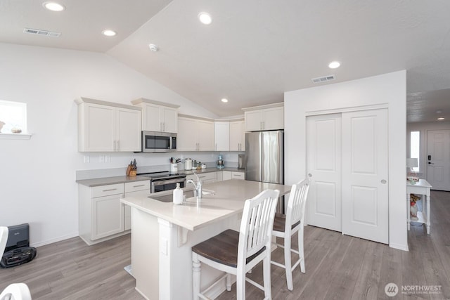 1205 W Sequoia Rd, Moses Lake, WA 98837 - kitchen with appliances with stainless steel finishes, lofted ceiling, light wood-type flooring, an island with sink, and white cabinetry