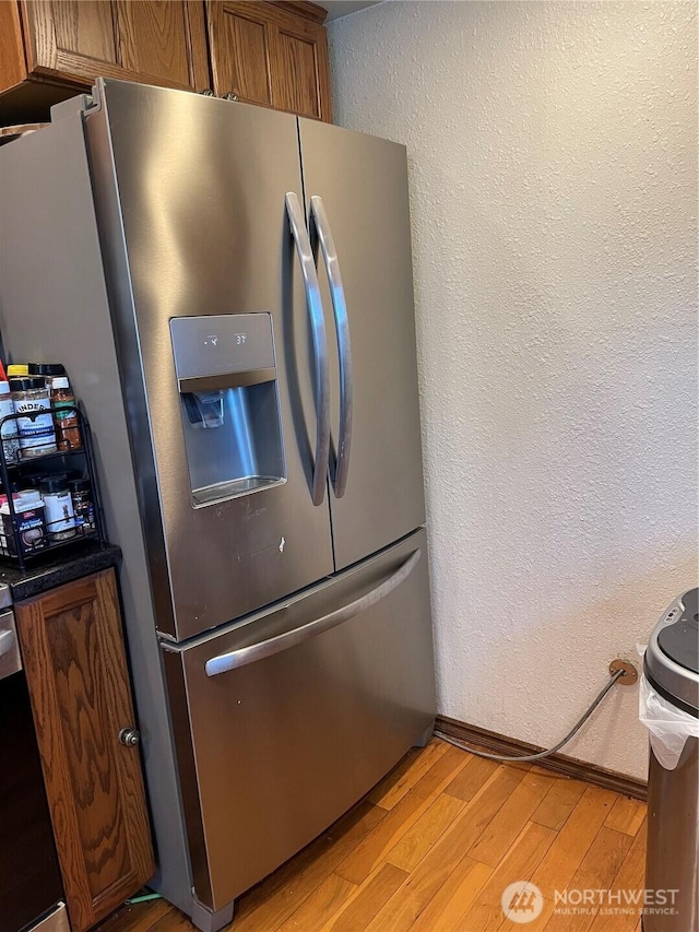 1610 M St NE, Auburn, WA 98002 - kitchen with stainless steel fridge, light wood-style floors, brown cabinetry, a textured wall, and dark countertops