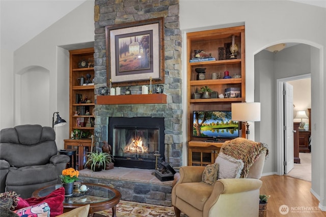 461 Klahhane Rd, Sequim, WA 98382 - living room with arched walkways, a stone fireplace, wood finished floors, built in shelves, and vaulted ceiling