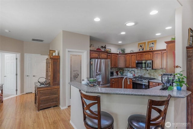 461 Klahhane Rd, Sequim, WA 98382 - kitchen with appliances with stainless steel finishes, light wood finished floors, a kitchen breakfast bar, backsplash, and a peninsula
