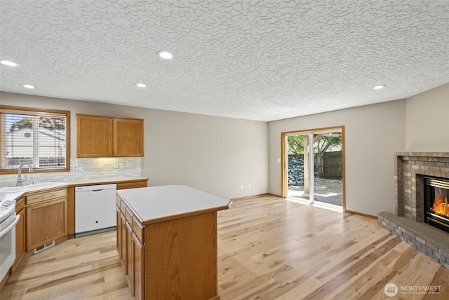 13019 NE 96th Way, Vancouver, WA 98682 - kitchen featuring white dishwasher, light wood finished floors, a fireplace, a kitchen island, and tasteful backsplash