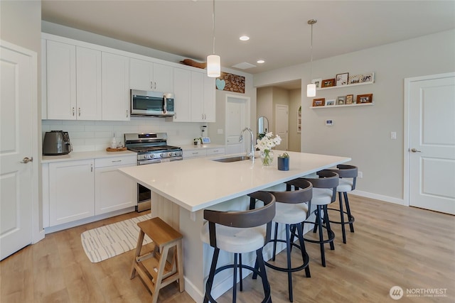 15539 Bergh Ct SE, Yelm, WA 98597 - kitchen featuring stainless steel appliances, light wood-style flooring, a kitchen island with sink, a breakfast bar, and white cabinetry