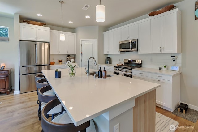 15539 Bergh Ct SE, Yelm, WA 98597 - kitchen with appliances with stainless steel finishes, a kitchen bar, light wood finished floors, decorative light fixtures, and recessed lighting