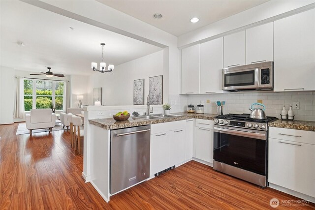 1899 NE Kenyon Ct, Issaquah, WA 98029 - kitchen with stainless steel appliances, a peninsula, open floor plan, wood finished floors, and white cabinets