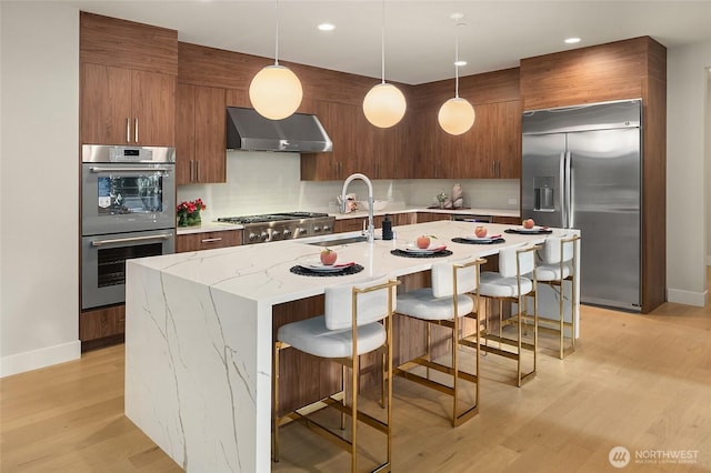 10915 126th Pl NE, Kirkland, WA 98033 - kitchen featuring wall chimney range hood, appliances with stainless steel finishes, modern cabinets, tasteful backsplash, and a kitchen breakfast bar