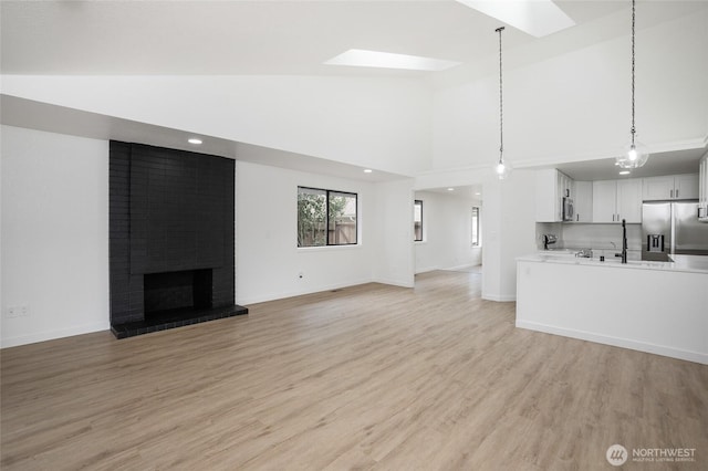 1308 133rd St S, Tacoma, WA 98444 - unfurnished living room featuring a skylight, light wood-type flooring, a brick fireplace, high vaulted ceiling, and recessed lighting