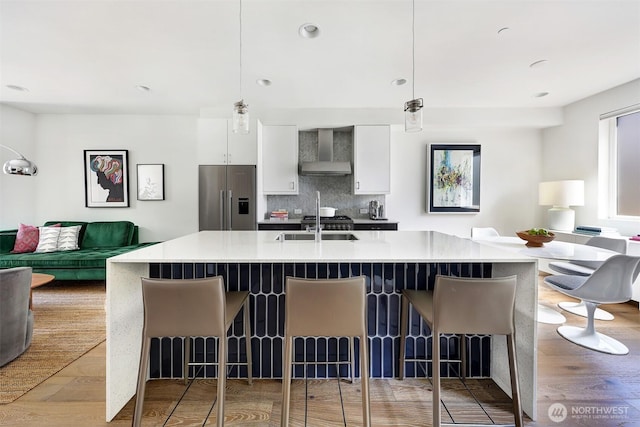 1117 34th Ave Unit B, Seattle, WA 98122 - kitchen featuring stainless steel fridge, wall chimney range hood, open floor plan, white cabinets, and tasteful backsplash