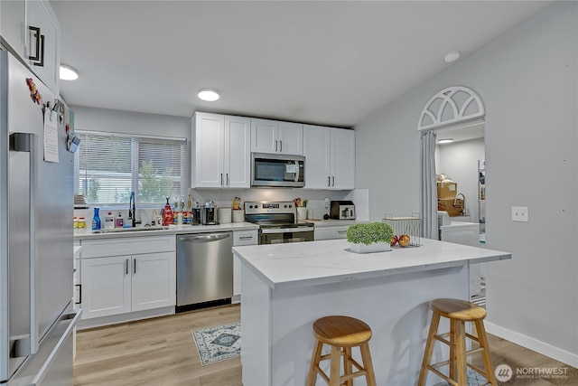 10707 209th Ave E, Bonney Lake, WA 98391 - kitchen with stainless steel appliances, a breakfast bar, light wood-style floors, white cabinetry, and light stone counters