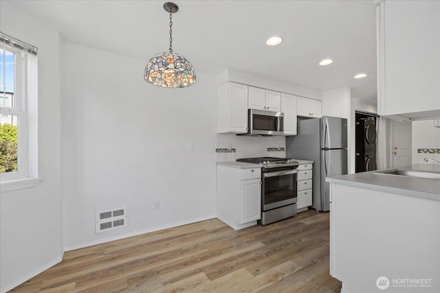 2448 NW 59th St Unit 301, Seattle, WA 98107 - kitchen featuring stainless steel appliances, stacked washer / drying machine, white cabinets, light wood-style flooring, and hanging light fixtures