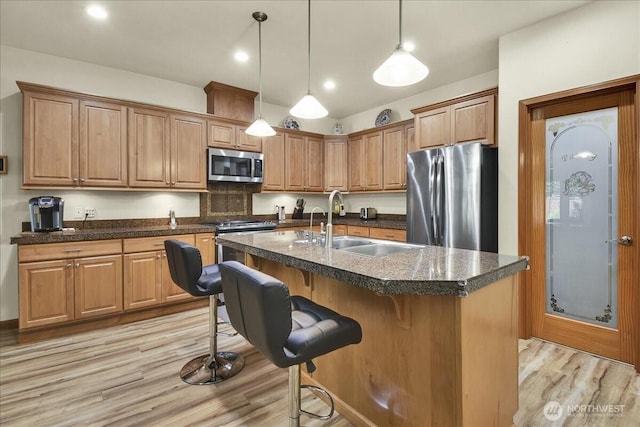15203 148th Avenue Ct E, Orting, WA 98360 - kitchen with appliances with stainless steel finishes, light wood finished floors, dark countertops, hanging light fixtures, and a center island with sink