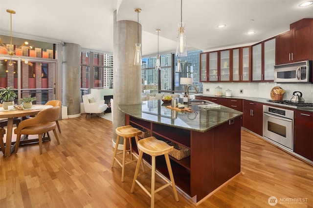 2033 2nd Ave Unit 703, Seattle, WA 98121 - kitchen with appliances with stainless steel finishes, light wood-type flooring, a kitchen breakfast bar, recessed lighting, and glass insert cabinets
