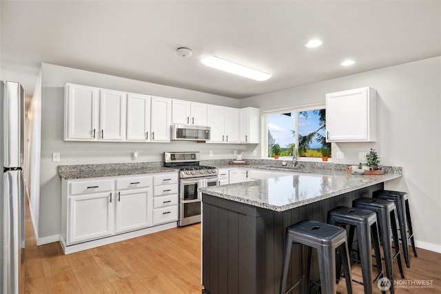 2141 Jason Ct, Ferndale, WA 98248 - kitchen with appliances with stainless steel finishes, a peninsula, a kitchen bar, white cabinets, and light stone counters