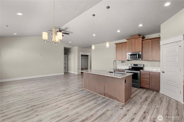 832 Q St SW, Quincy, WA 98848 - kitchen with stainless steel appliances, light wood-style floors, vaulted ceiling, open floor plan, and brown cabinetry