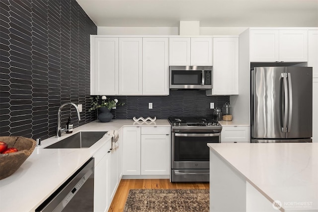 6042B 41st Ave SW, Seattle, WA 98136 - kitchen with appliances with stainless steel finishes, white cabinetry, light countertops, light wood-style flooring, and decorative backsplash