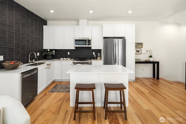 6042B 41st Ave SW, Seattle, WA 98136 - kitchen with stainless steel appliances, a center island, light countertops, a kitchen bar, and light wood-style floors