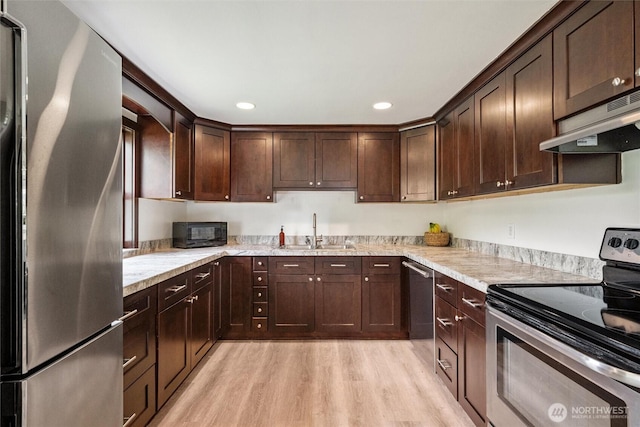 17371 Dunbar Rd, Mount Vernon, WA 98273 - kitchen featuring appliances with stainless steel finishes, light wood-type flooring, under cabinet range hood, dark brown cabinets, and light stone countertops