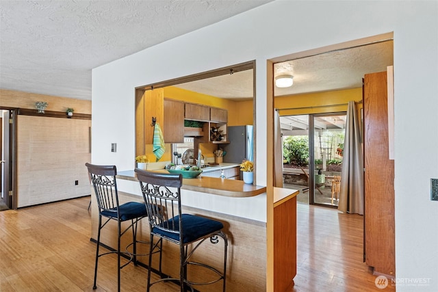 152 E Park Ln, Port Angeles, WA 98362 - kitchen with light wood-style flooring, freestanding refrigerator, a textured ceiling, light countertops, and a breakfast bar